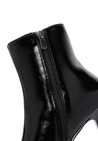 Stivale alla caviglia in vernice nera con zip laterale, texture liscia e design elegante con tacco alto.