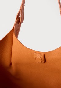 Pehme tekstuuriga oranž nahast kott õmmeldud rihma ja trukk-kinnitusega, valgel taustal.