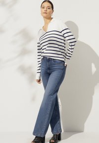 Witte en marineblauwe gestreepte trui met kraag, gecombineerd met blauwe flared jeans en zwarte open-toe sandalen met hak. Soepele textuur, casual ontwerp.