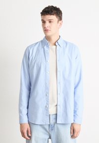 Lichtblauw langemouw shirt van katoen, met een button-down kraag en witte knopen, gelegd over een crèmekleurig top.