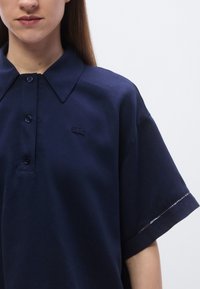 Polo bleu marine en coton, avec un col classique, trois boutons et un petit logo brodé sur la poitrine gauche. Manches courtes.