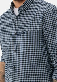 Camicia con bottoni caratterizzata da un motivo a quadri blu e nero, colletto, maniche lunghe e una tasca sul petto con dettaglio di cucitura.