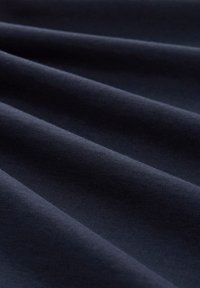 Mørkeblå stoff med en jevn tekstur, som har myke folder som reflekterer lys, og fremhever den jevne vevingen og den uniforme fargen.