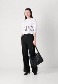 White cropped t-shirt with "CALVIN" in black print, paired with black wide-leg trousers. Black leather shoulder bag, black pointed heels.