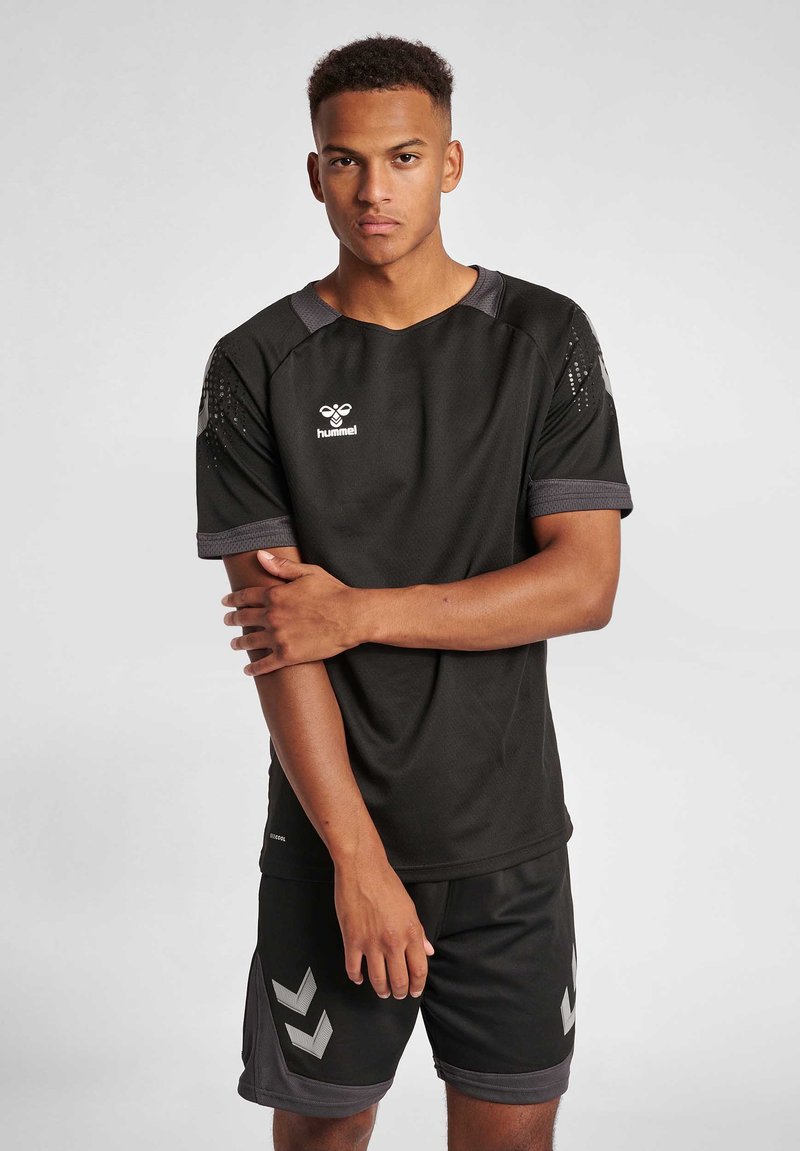 Zwart sportshirt met korte mouwen, grijze accenten en logo op de borst, gecombineerd met zwarte shorts met een grijs chevronpatroon.