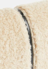 Tessuto beige testé con un aspetto morbido e peloso, accentuato da un dettaglio in pelle nera liscia lungo la cucitura.