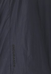 Merin tuulenpitävä takki, jossa on kestävä, kevyt kangas ja sileä pinta. "ENDURANCE" -logo painettuna mustana sivusaumaan.