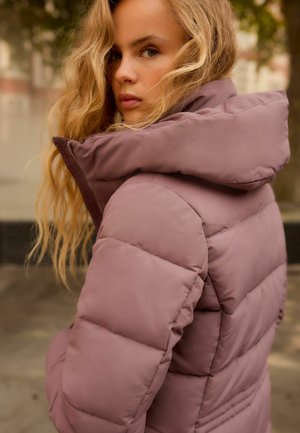 Doudoune mauve clair avec un col haut, en tissu lisse. Inclut des sections matelassées et une fermeture éclair à l'avant.