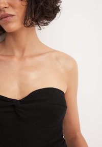 Must mustriba top mustrisest tekstuuriga ja keerutamise detailiga rinnaosas. Üksikasjalik, keha lähedane kuju rõhutab kaela ja õlgade jooni.