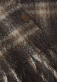 Écharpe en laine à carreaux marron et crème avec des bords frangés et une étiquette en cuir. Texture douce avec une apparence chaleureuse.