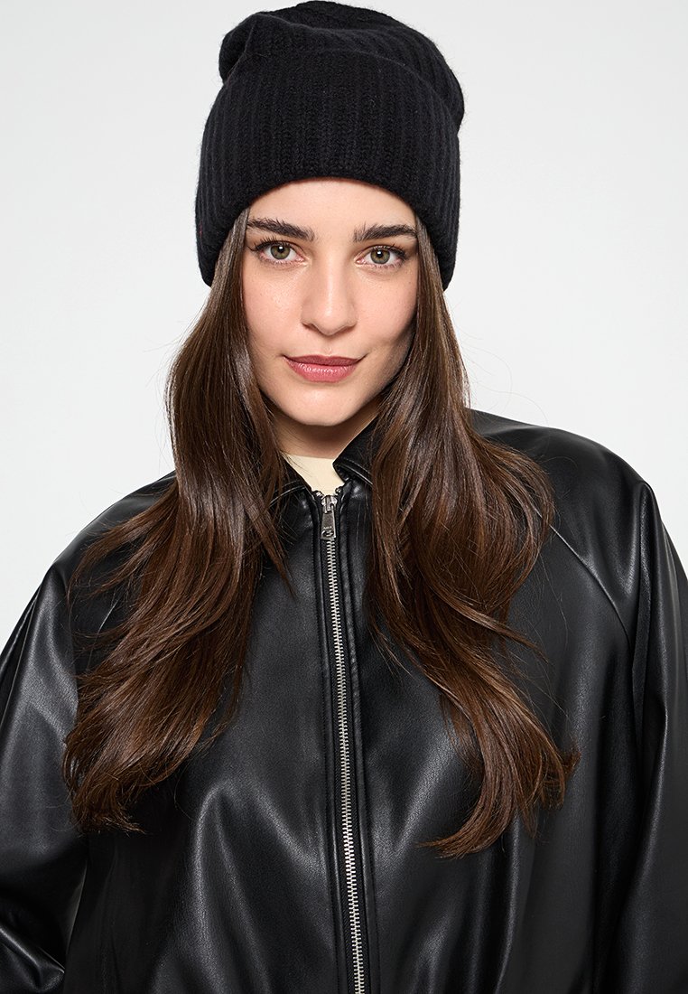 Czarna dziana czapka, prążkowana faktura, w połączeniu z błyszczącą czarną skórzaną kurtką z zapięciem na zamek i szerokimi ramionami.