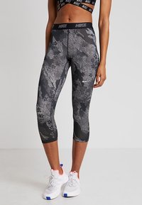 Czarne legginsy capri marki Nike z teksturowanym wzorem, które mają szaro-białe akcenty, wysoki stan oraz materiał odprowadzający wilgoć.