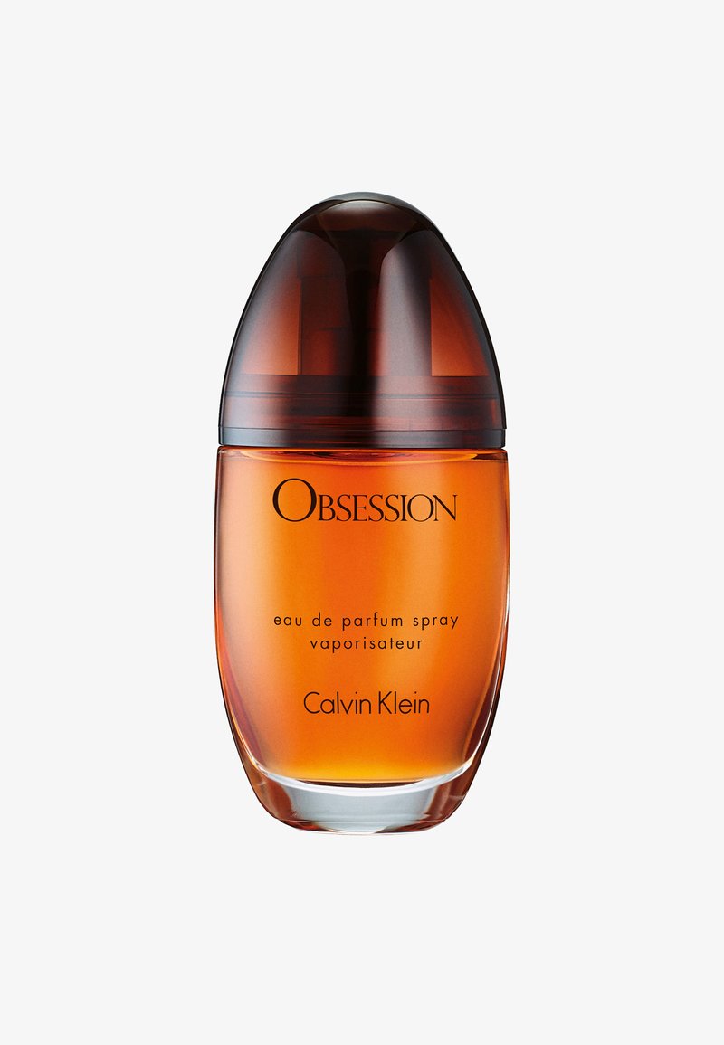 Flacon de parfum en verre ambré avec un bouchon brun foncé étiqueté Obsession eau de parfum spray par Calvin Klein.