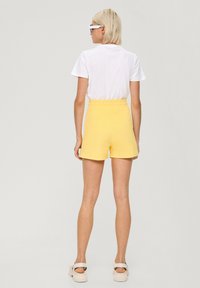 Geel katoenen shorts met een elastische tailleband, met een losse pasvorm en een gladde textuur. Gstyled met een wit t-shirt en lichtgekleurde schoenen.