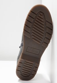 Šedá podešev boty s gumovou texturou, která má hluboké vzory, vyražené logo a hladký, pevných hnědý základ.