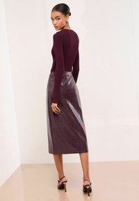 Burgundska rebrasta majica s dugim rukavima uparena s sjajnom midi suknjom s uzorkom krokodila. Chic cipele s visokom potpeticom upotpunjuju odjevnu kombinaciju.