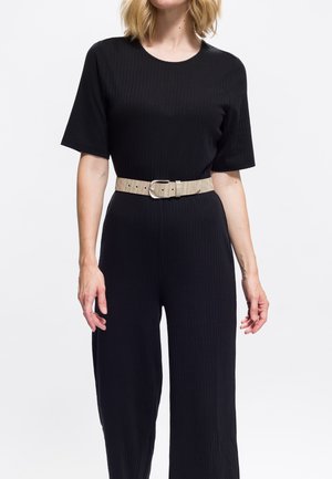 Musta ribbineuloksinen haalari, jossa on lyhyet hihat ja leveä beigen värinen vyö metallisoljella. Kangas on teksturoitu kuviolla.