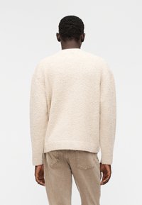 Μπεζ πουλόβερ με υφή, άνετη εφαρμογή, στρογγυλή λαιμόκοψη και μακριά μανίκια, σε συνδυασμό με ανοιχτό καφέ τζιν. Απαλή πλεκτή ύλη.