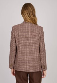 Blazer à motif écossais marron et beige avec une coupe structurée, des revers crantés et des poignets à bouton. Comprend une fente arrière unique.