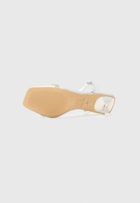 Transparent klacksandaler med silverfärgade remmar, en beige gummisula och strukturerat mönster. Har en spänne-stängning och en genomskinlig tårem.