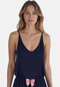 Sötétkék tank top mély V-nyakkal és vékony pántokkal, rózsaszín masni díszítéssel a deréknál ellátott sorttal párosítva. Puha anyag és laza szabás.