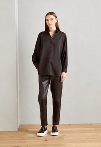Black long-sleeve shirt with buttons, paired with fitted black leather pants and black slip-on sneakers with white soles. Smooth textures throughout.