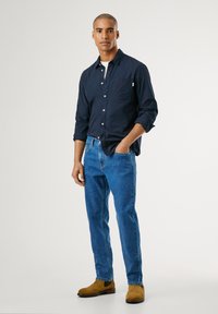 Sötétkék gombos ing, mellzsebbel, kék farmernadrág és világosbarna velúr csizma. Slim fit, sima textúra, laza kialakítás.