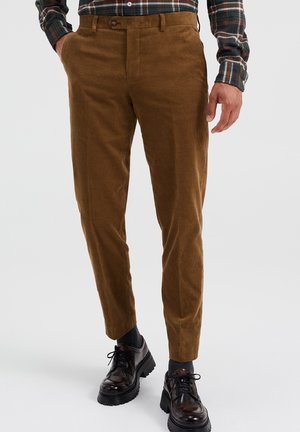 Ruskeat ribbineuloshousut, jotka on yhdistetty ruudulliseen paitaan, joka on sullottu housuihin. Yhdistetty tummien sukkien ja kiillotettujen mustien nauhallisten kenkien kanssa.