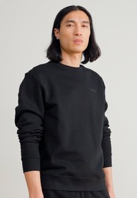 Maglione girocollo nero realizzato in tessuto morbido, con polsini e orlo a costine, e un sottile dettaglio del logo sul petto.
