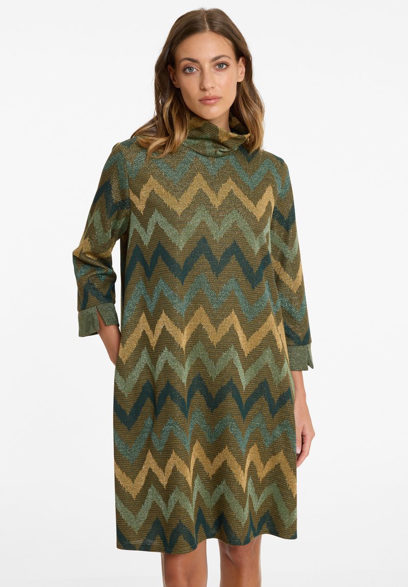 Robe longueur genou avec col drapé, ornée d'un motif en chevron dans des tons de vert, doré et marron. Fabriquée en tissu texturé légèrement brillant.