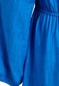 Zila kleita no faktūras auduma ar garām piedurknēm un elastīgu vidukļa jostu, visa materiāla gareniskās svītras.