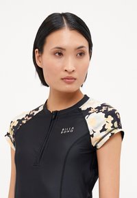 Black short-sleeve wetsuit featuring floral print accents on the shoulders, zip front, and the brand logo "BILLA BONG" on the chest.