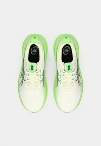 Chaussures de sport légères avec une tige crème, des accents vert néon, un logo noir et des détails réfléchissants ; présentent une surface texturée et une fermeture à lacets.