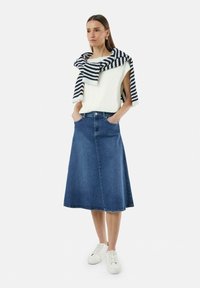 Jupe en denim en forme A, de couleur bleu foncé, longueur genou, avec poches et finitions soignées. Portée avec un haut sans manches blanc et un pull rayé bleu marine.