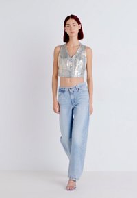 Silver metallic cropped vest top, high-waisted light blue jeans, and clear strappy sandals. Smooth texture and relaxed fit.