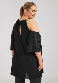 Top nero a spalle scoperte con maniche a campana, tessuto texturizzato, dettaglio con gancio sul retro e vestibilità comoda, con una leggera lucentezza.