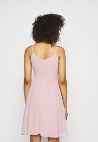 Růžové šaty s tenkými ramínky, přiléhavým trupem a rozšířenou sukní. Na zadní straně je malý zip a hladký materiál. Jednoduchý design.