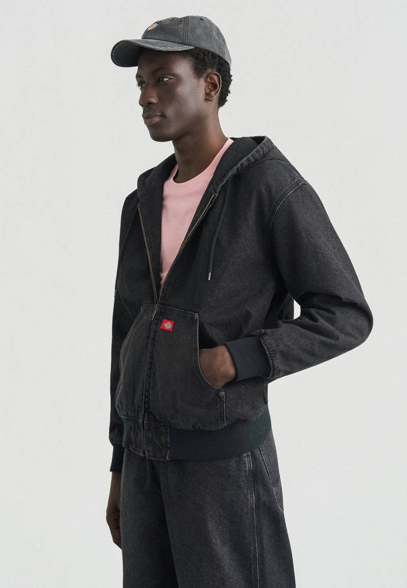 Γκρι τζιν μπουφάν με φερμουάρ και μπροστινές τσέπες, με μανσέτες με ρίγες και κόκκινη ετικέτα. Συνδυασμένο με ροζ μπλουζάκι και ταιριαστό γκρι παντελόνι.