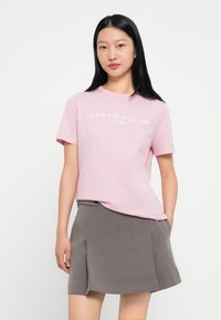Svetloružová bavlnená tričko s bielym logom "TOMMY HILFIGER", s okrúhlym výstrihom a krátkymi rukávmi; skombinované so šedou plisovanou sukňou.