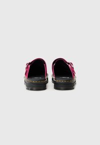Pink suede backless shoes with black soles and yellow stitching, featuring adjustable buckles and cushioned insoles.