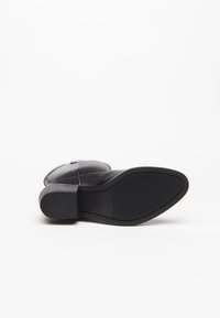 Stivaletto in pelle nera con tacco spesso, presenta una tomaia liscia e una suola in gomma testurizzata per un grip migliore. Design minimalista con linee pulite.