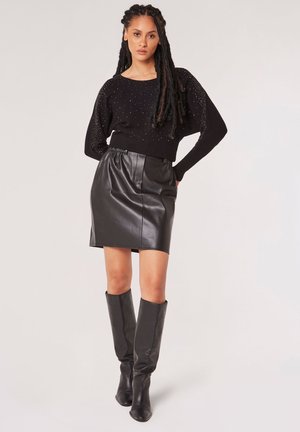Maglione nero a maglia con dettagli testurizzati, abbinato a una mini gonna a tubino in pelle nera e stivali al ginocchio in pelle nera.