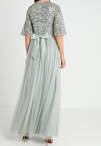 Lång, ljusgrå klänning med en paljettbeströdd bodice, korta ärmar och en flödande tyllkjol. Har en rosett detalj på baksidan.