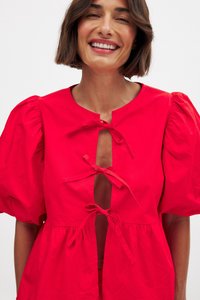 Robe en coton rouge avec manches bouffantes, ouverture en trou de serrure à l'avant et accents noués. Design évasé avec taille froncée.
