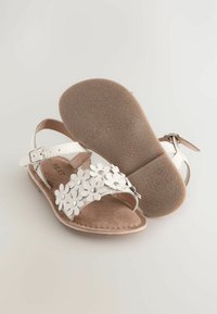 Sandalo bianco con un design floreale sulla fascia, suola texturizzata marrone, cinturino alla caviglia regolabile e soletta in morbido suede.