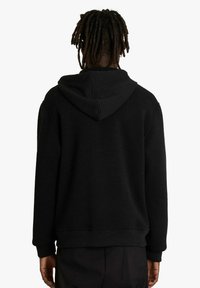 Felpa nera con cappuccio regolabile con cordino, polsini e orlo a coste. Presenta un tessuto lavorato e una vestibilità comoda. La vista posteriore mostra lo scollo e la forma.
