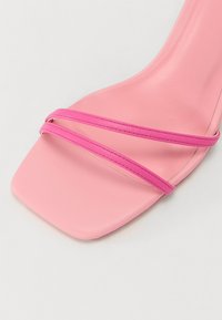 Sandal con tacco alto rosa caratterizzata da una punta quadrata, cinturini stretti di un rosa più scuro e una finitura opaca liscia su una suola leggera.