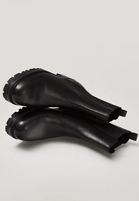 Paire de bottines Chelsea en cuir noir avec semelles en caoutchouc épaisses et panneaux latéraux élastiques, présentées sur un fond gris clair.