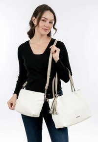 Sacs à main blancs avec une texture lisse ; l'un présente un accent de frange. Anslesbeige réglables et un design élégant. Modèle portant un haut noir.