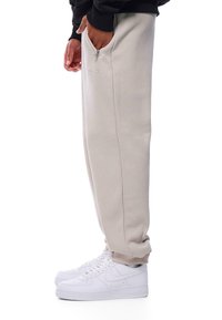 Beige sweatpants med afslappet pasform, elastiske manchetter og sidelommer, parret med hvide sneakers med perforerede detaljer.